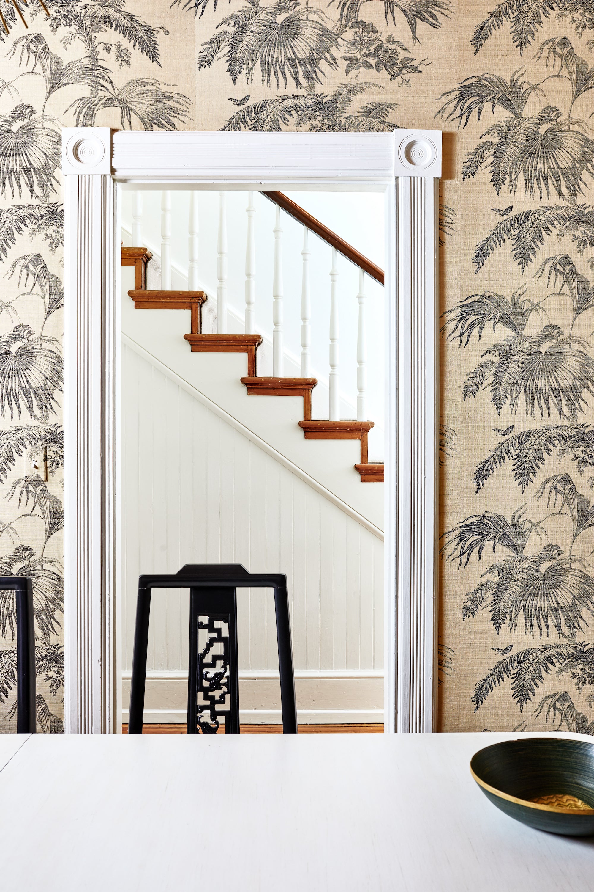 A wallpapered dining area looks into a hallway, in a home by Lisa & Leroy.