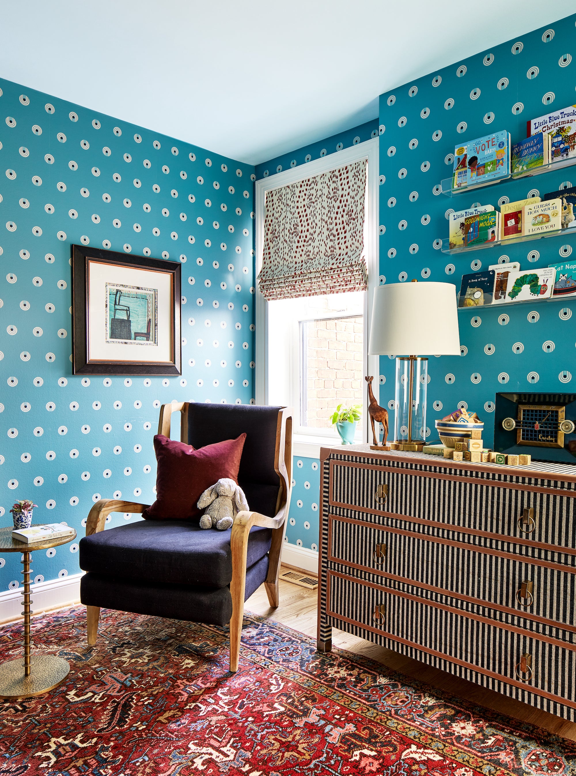 A playful nursery by Lisa & Leroy featuring wallpapered walls and a vintage rug.