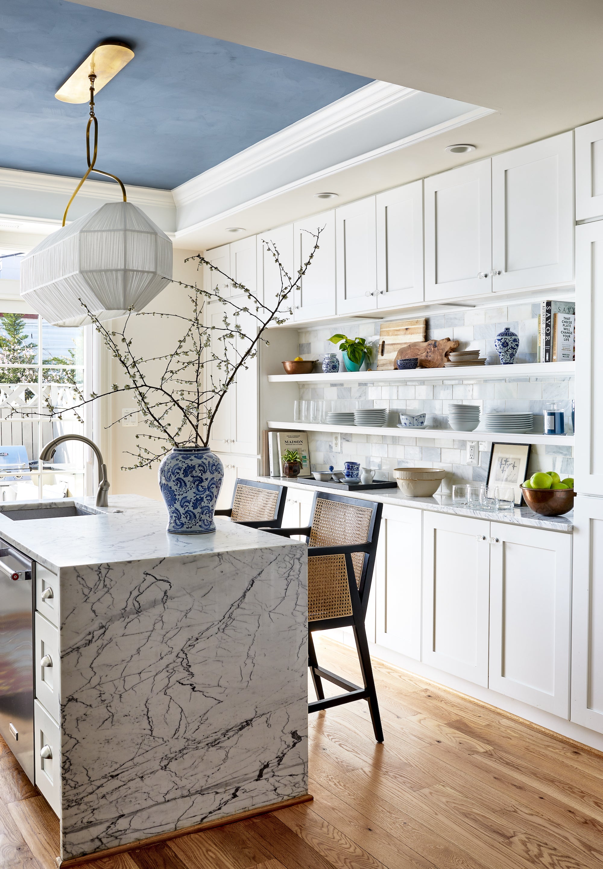 A kitchen by Lisa & Leroy with veiny marble, ceramic tile, and accents of blue.