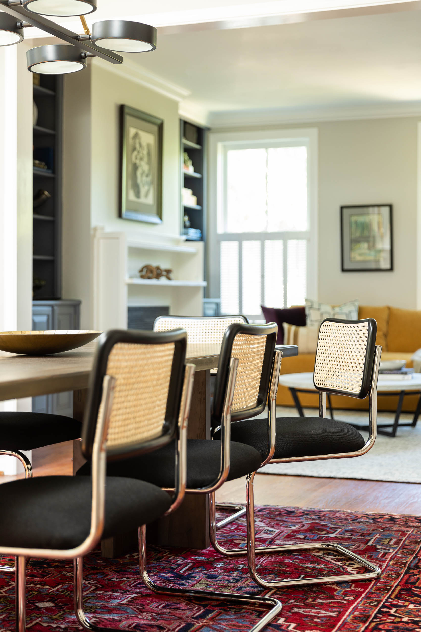 A dining room with a modern wood table, black cesca chairs, and a vintage rug, designed by Lisa & Leroy.