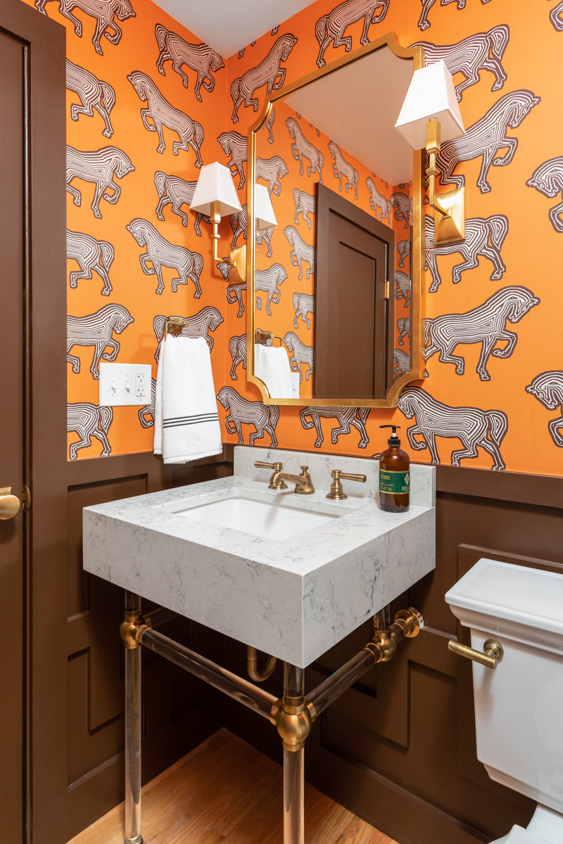 A bold powder bath by Lisa & Leroy with a marble pedestal sink, patterned wallpaper, and rich brown millwork.
