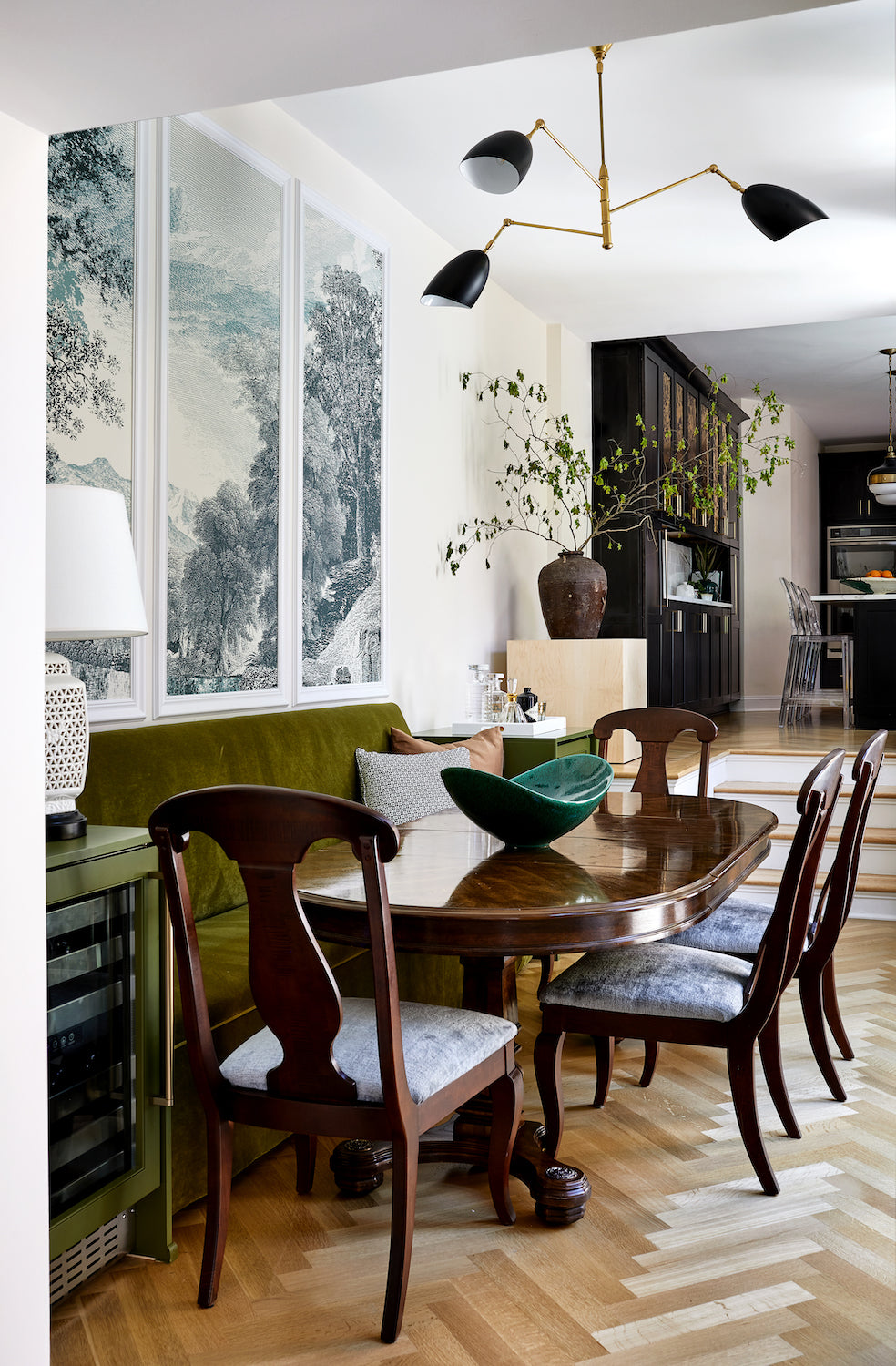 A landscape triptych over a dining area featuring an upholstered banquette, designed by Lisa & Leroy.