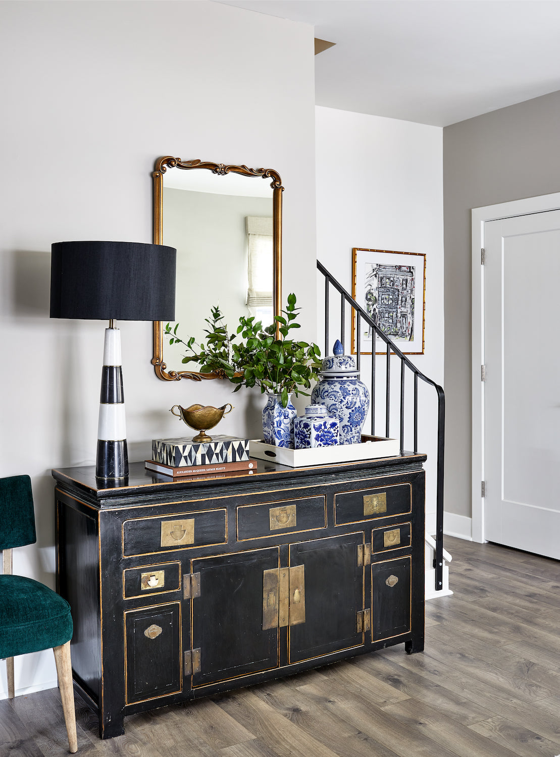 An entryway featuring a black antique cabinet styled with well-traveled decor, by Lisa & Leroy.